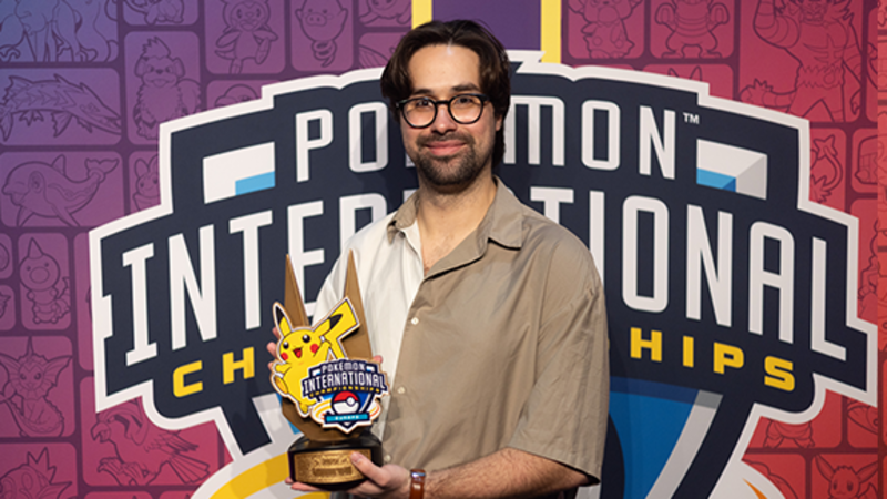 Wolfey Glick holding a trophy in front of the pokemon international backdrop